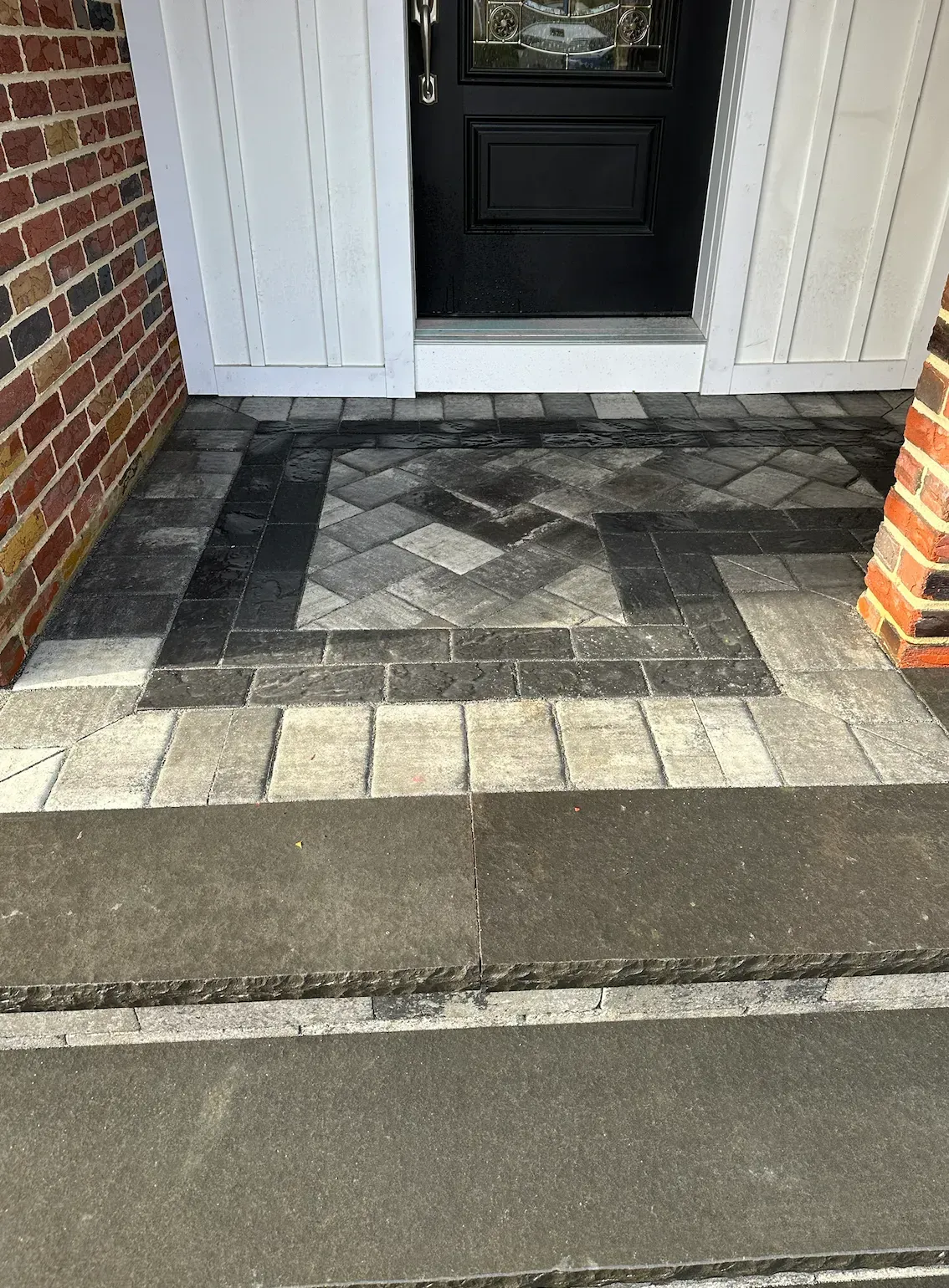 Brick entry with patterned pavers in front of a black door.