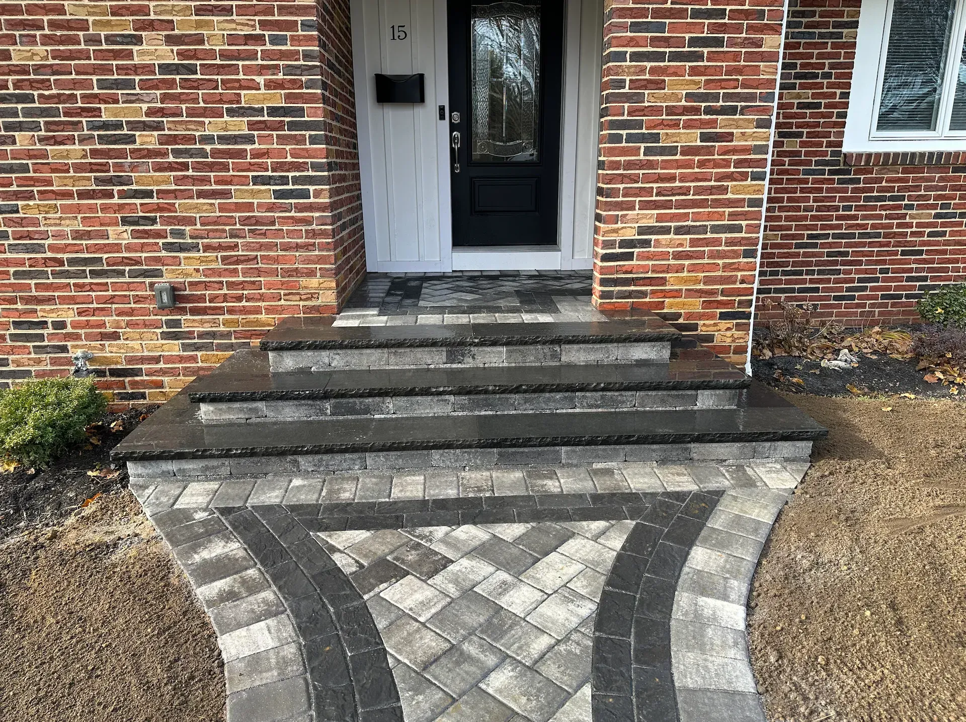 Brick home with paved walkway and steps leading to a black door.