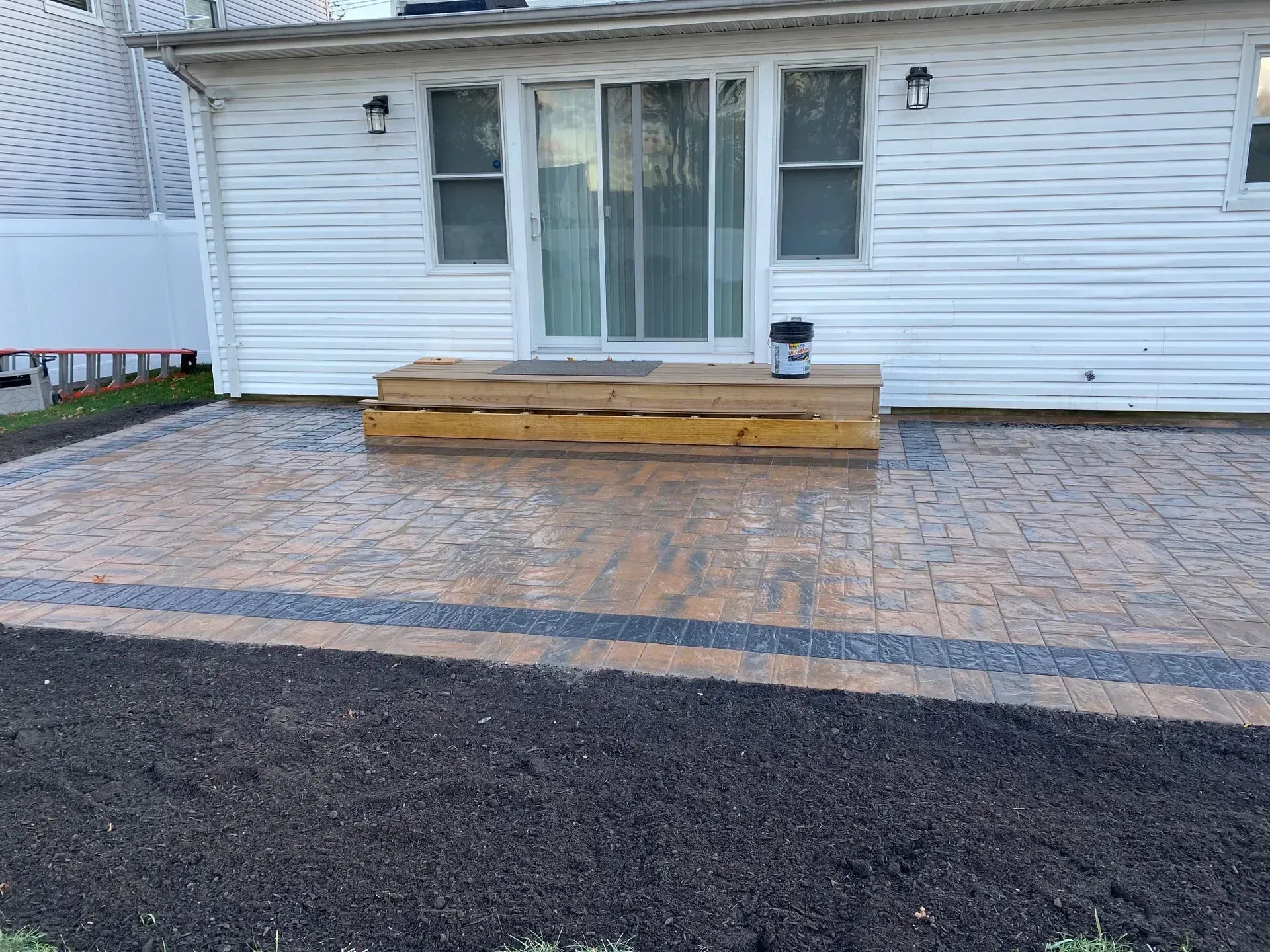 Brick patio with wooden steps leading to a white house with a sliding glass door.
