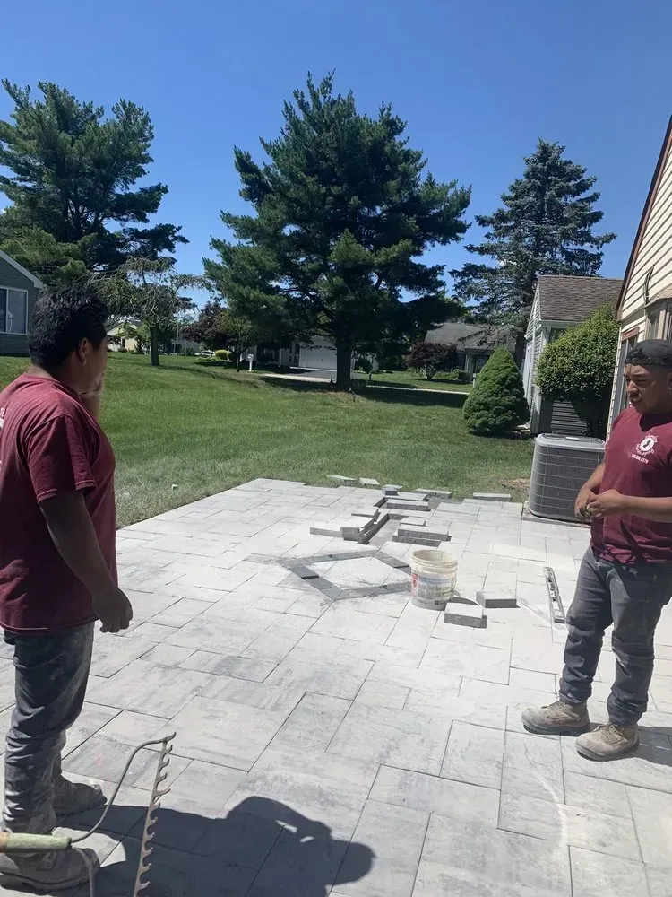 Two workers discussing the progress of laying pavers on a patio in a backyard setting.