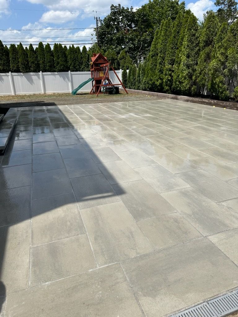 A person digs a trench in a backyard near a small excavator, a tree, and a house.