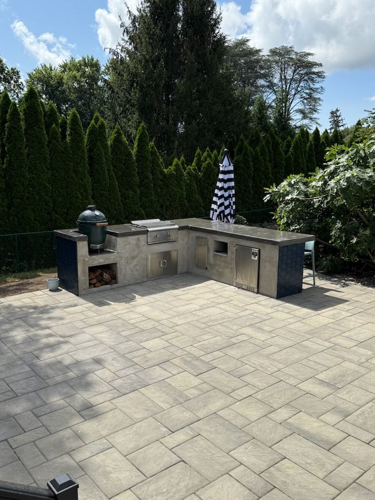 A person digs a trench in a backyard near a small excavator, a tree, and a house.