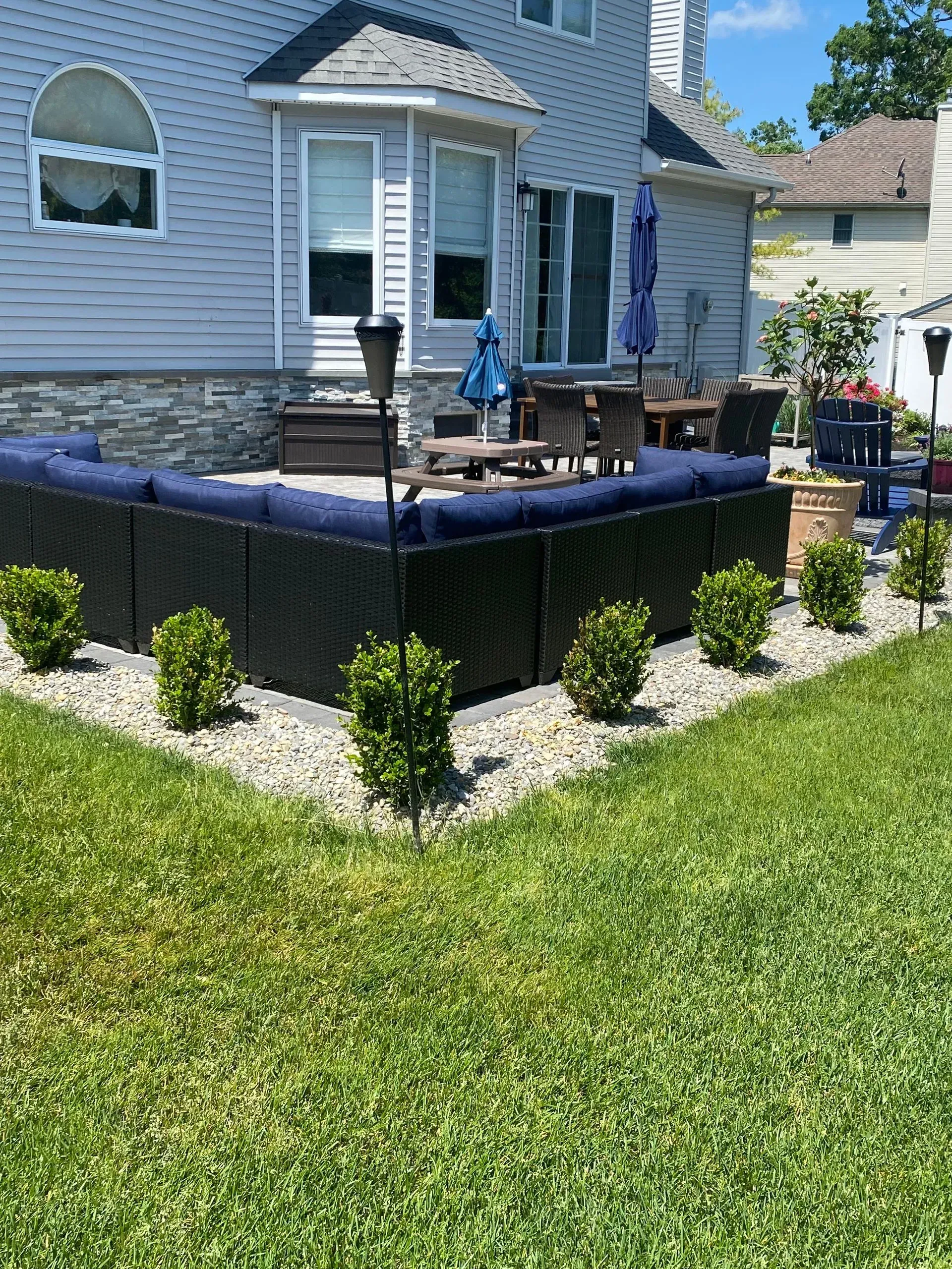 Backyard patio with blue cushions, boxwood shrubs, and gray gravel.