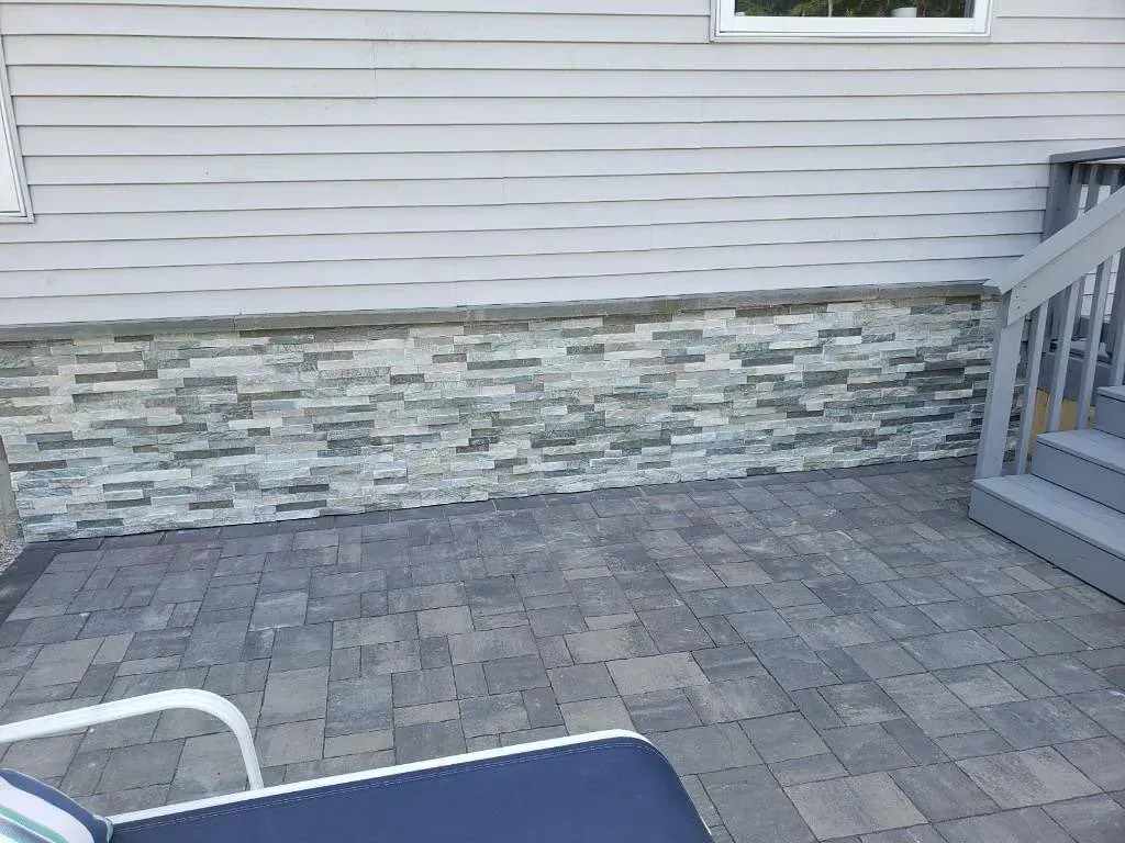 Gray brick patio beside a house with stone veneer siding, and a deck with gray steps.