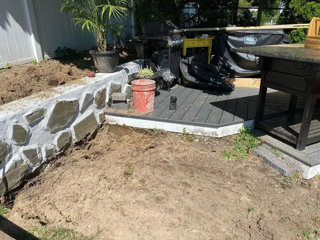Trench dug in a grassy yard, leading to a house with black siding, and an electrical box.