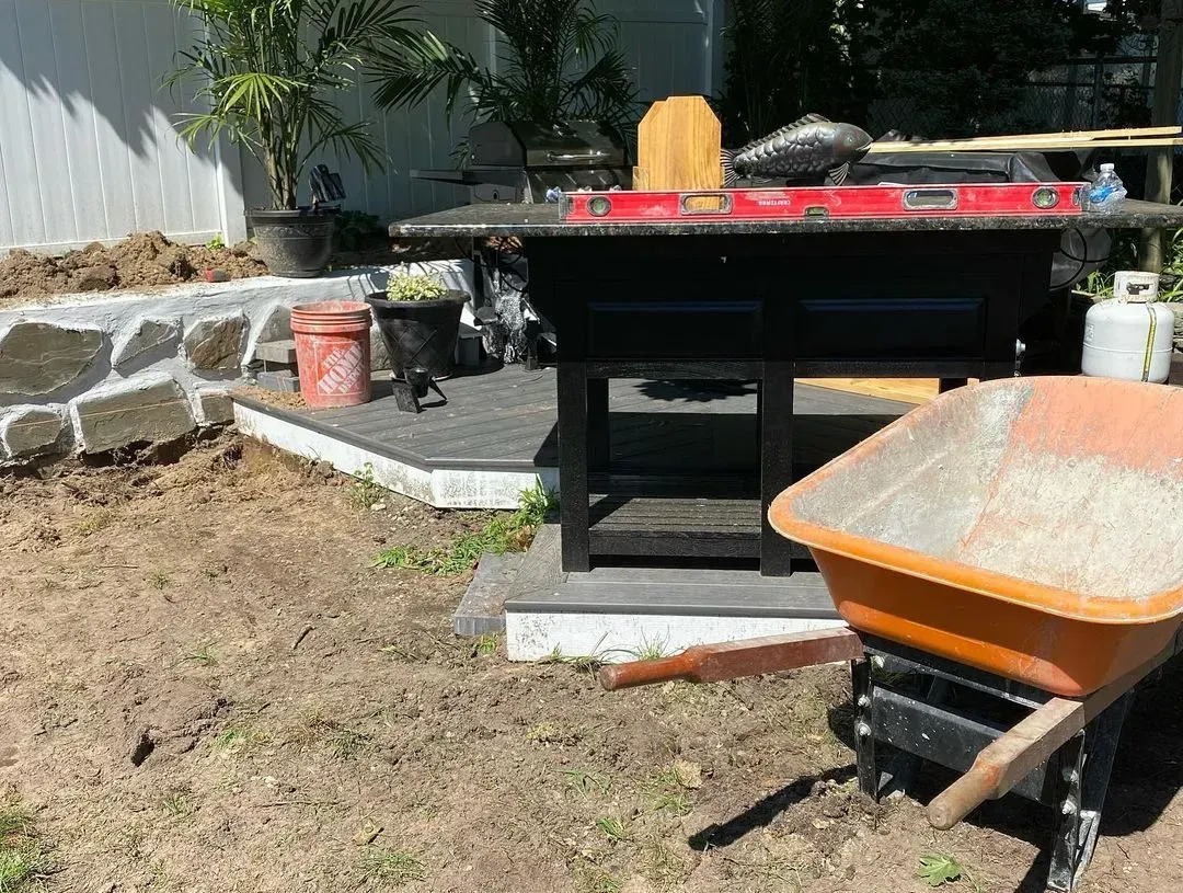 Outdoor workspace with grill, wheelbarrow, retaining wall, and tools.