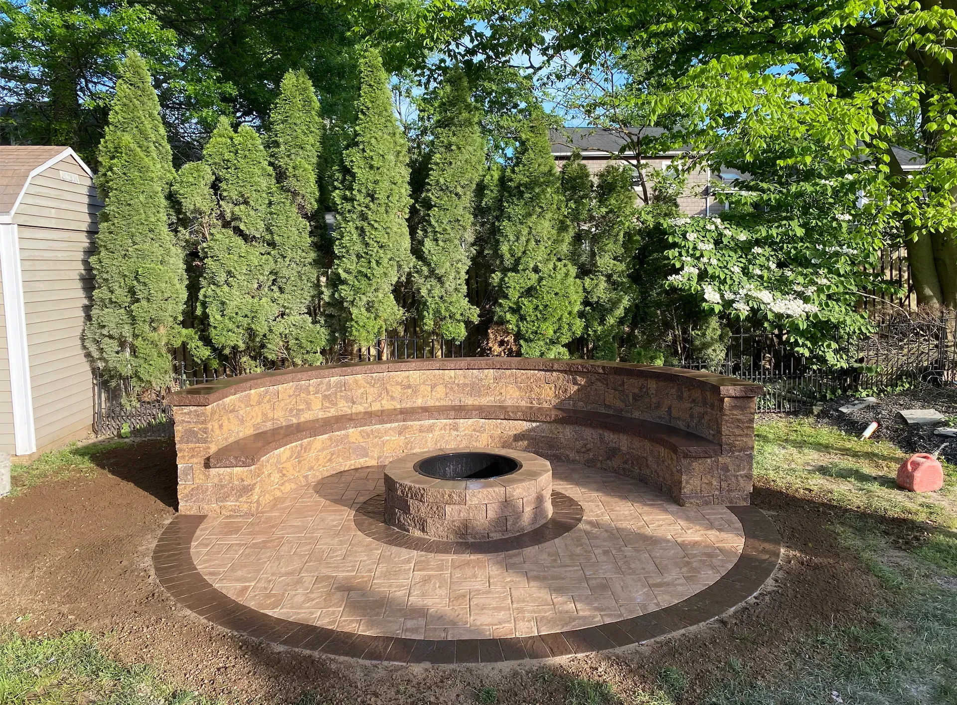 A person digs a trench in a backyard near a small excavator, a tree, and a house.