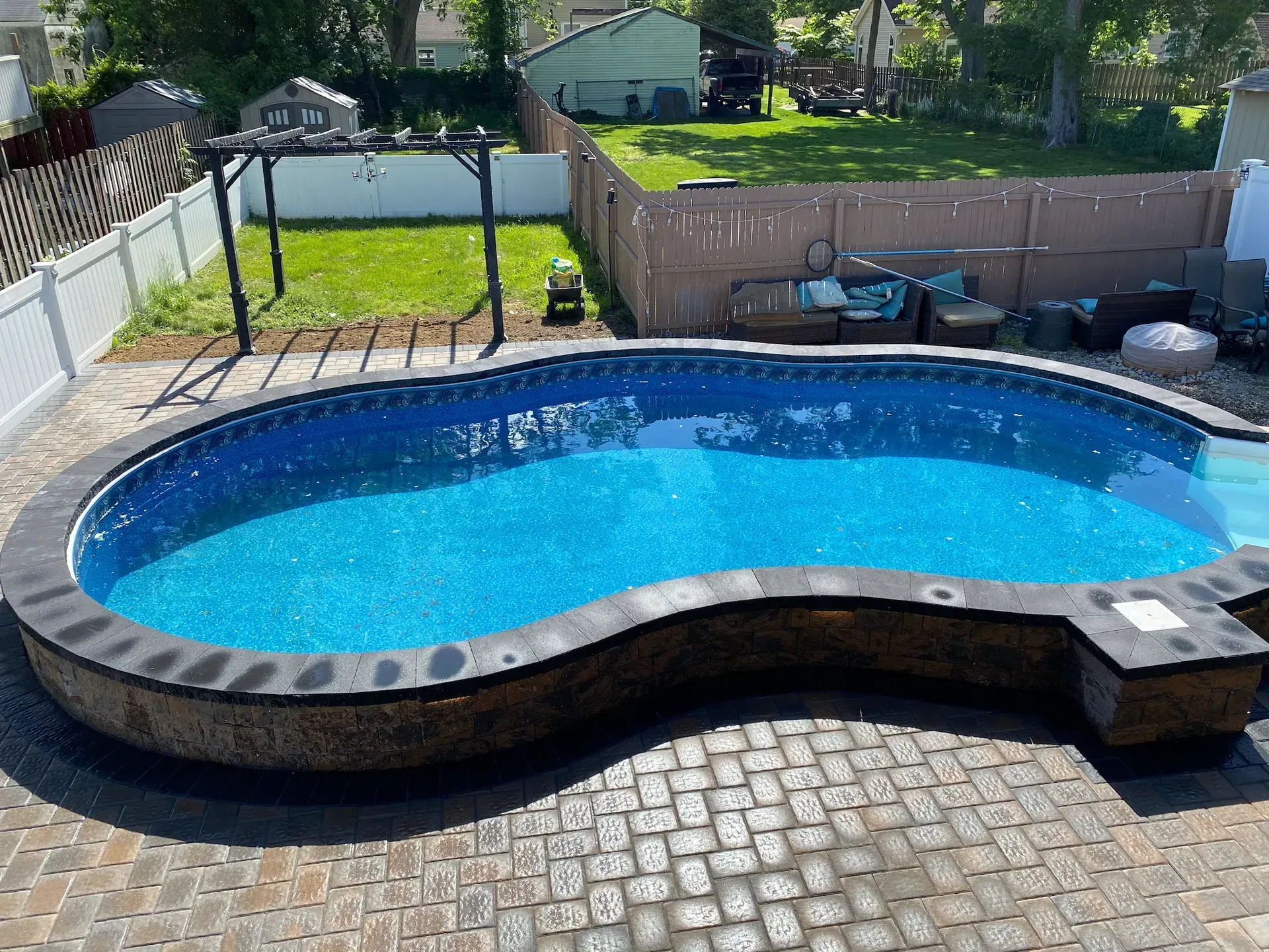 Backyard pool with blue water, surrounded by patio and lawn, bordered by fence.