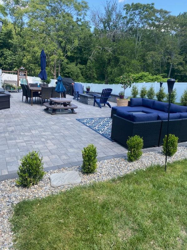 Patio with blue furniture, dining table, fire pit, and small shrubs.