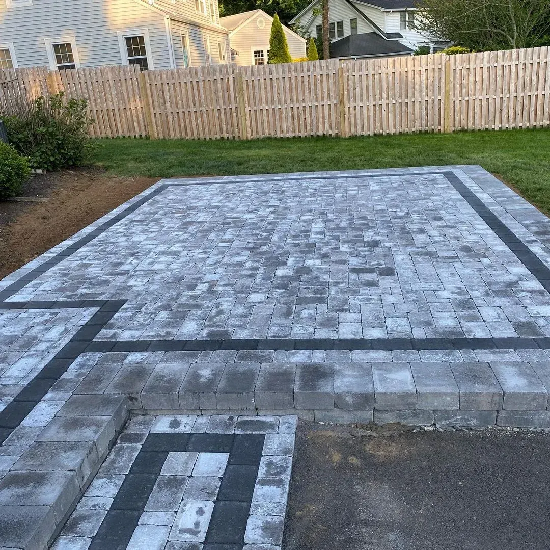 Close-up of gray paving bricks being laid on gravel base in a herringbone pattern.
