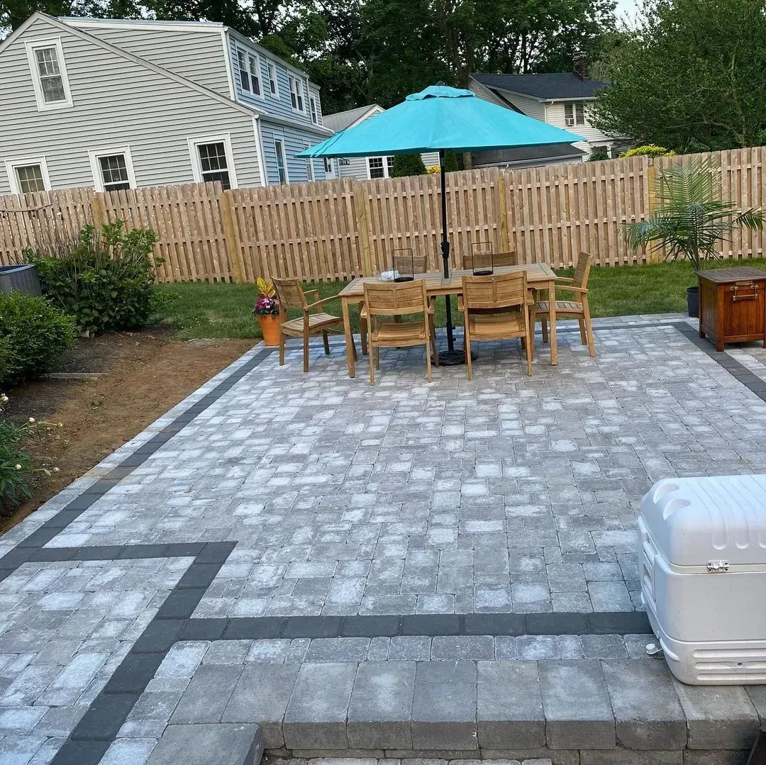 Patio with dining set, umbrella, and a light blue umbrella. Fenced backyard with a house in the background.
