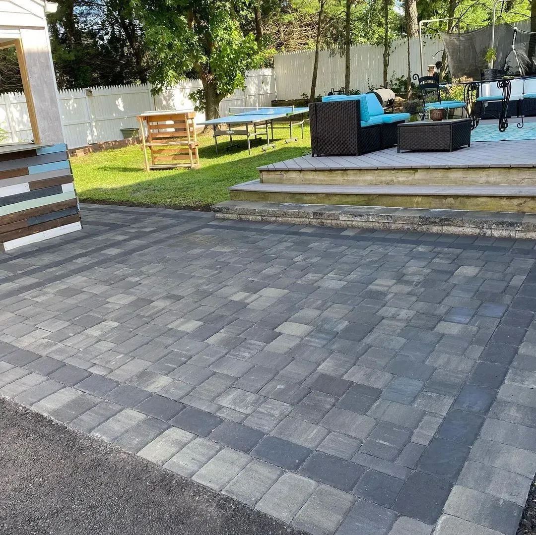 Brick driveway leading towards a two-story brick house with a white fence in the background.