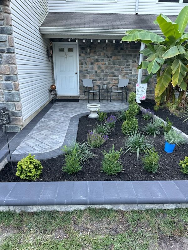 Front porch with stone walkway, small shrubs in black mulch, and a birdbath.