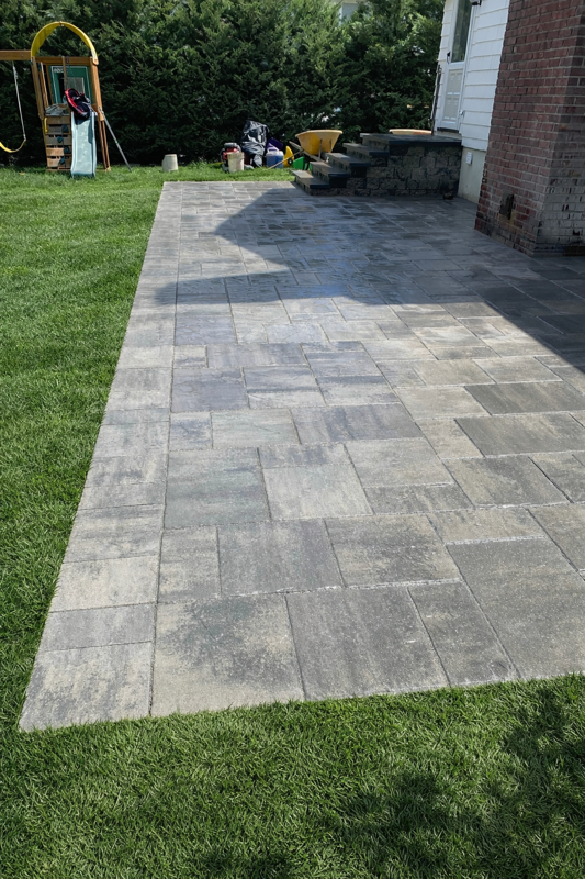 Stone paver patio next to green lawn, with steps leading to a house.