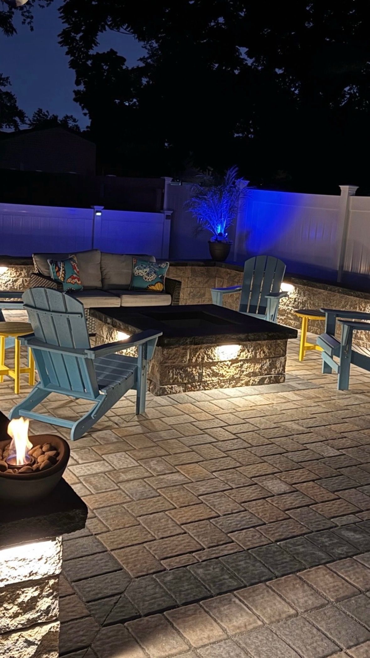 A person digs a trench in a backyard near a small excavator, a tree, and a house.