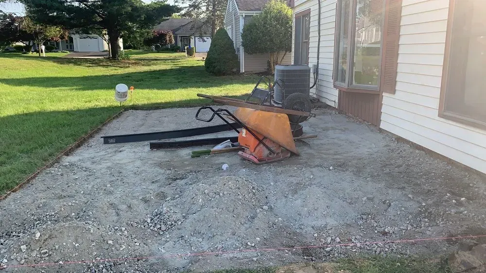 A gravel patio next to a house with construction equipment. Green grass and trees in the background.
