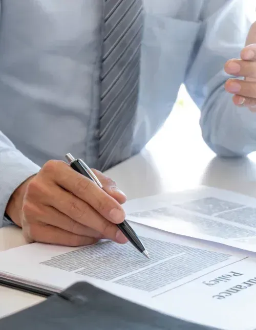 Person in a light blue shirt and tie pointing at insurance policy, in an office setting.