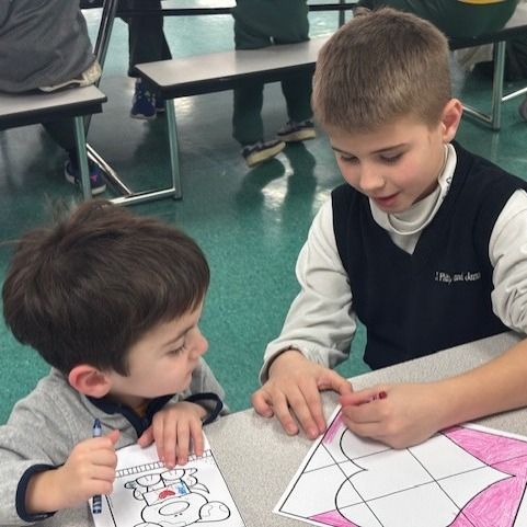 Two young boys are sitting at a table looking at a piece of paper