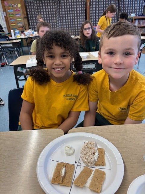 A boy and a girl are sitting at a table with a plate of food on it.
