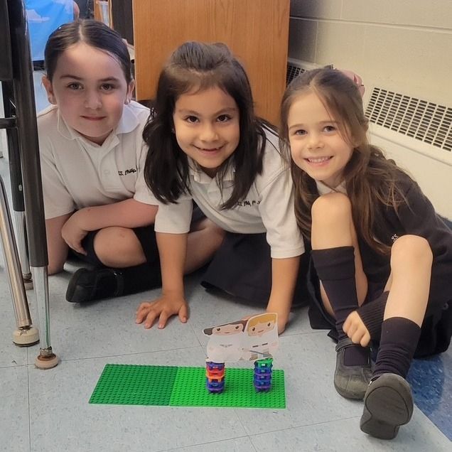 Three young girls are sitting on the floor in front of a lego display