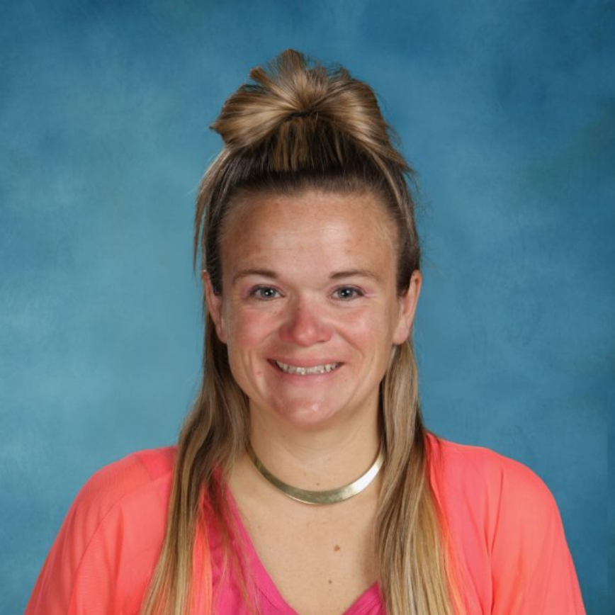 A woman wearing a necklace is smiling in front of a brick wall
