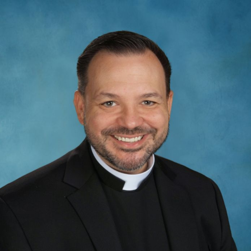 A man wearing a clergy collar is smiling for the camera