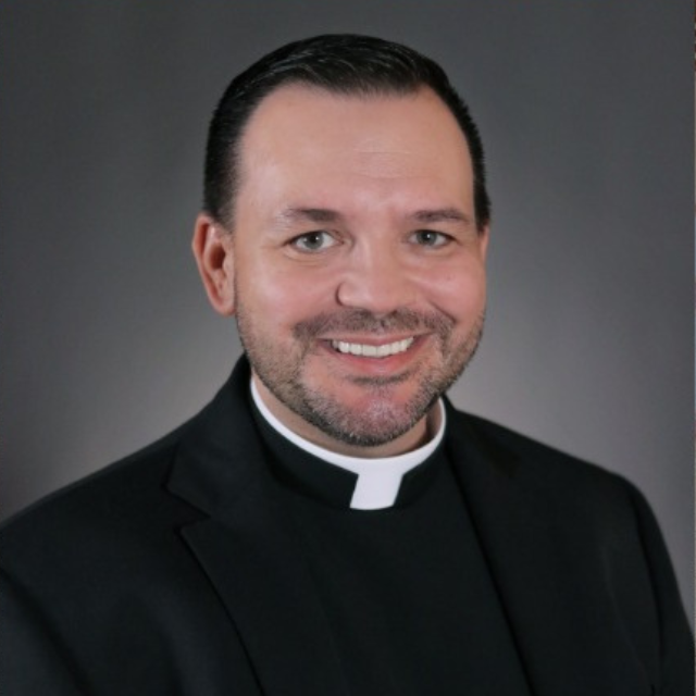 A man wearing a clergy collar is smiling for the camera