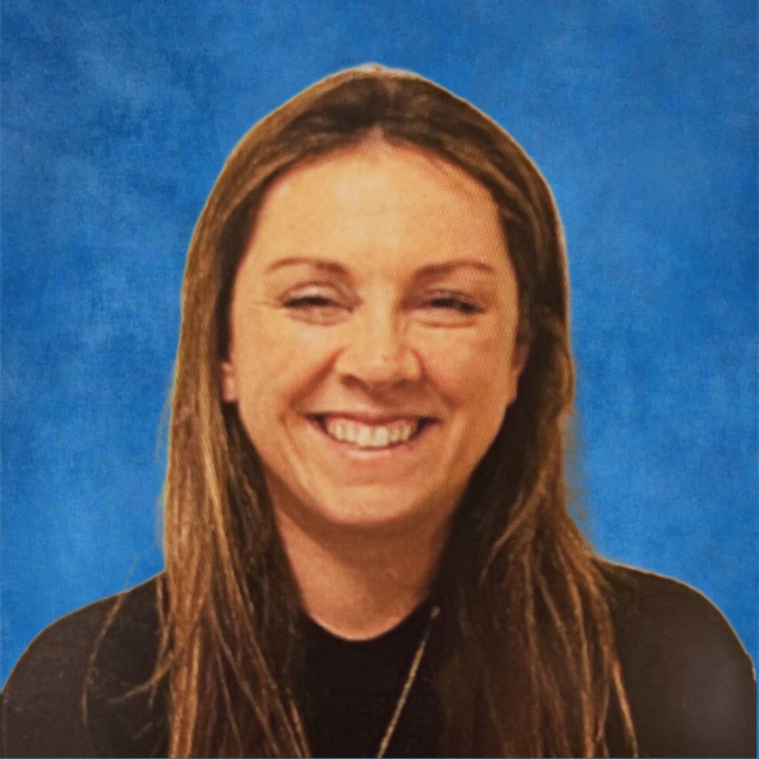 A woman with long hair is smiling in front of a brick wall.