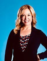 Smiling woman in a black blazer and patterned top against a bright blue background