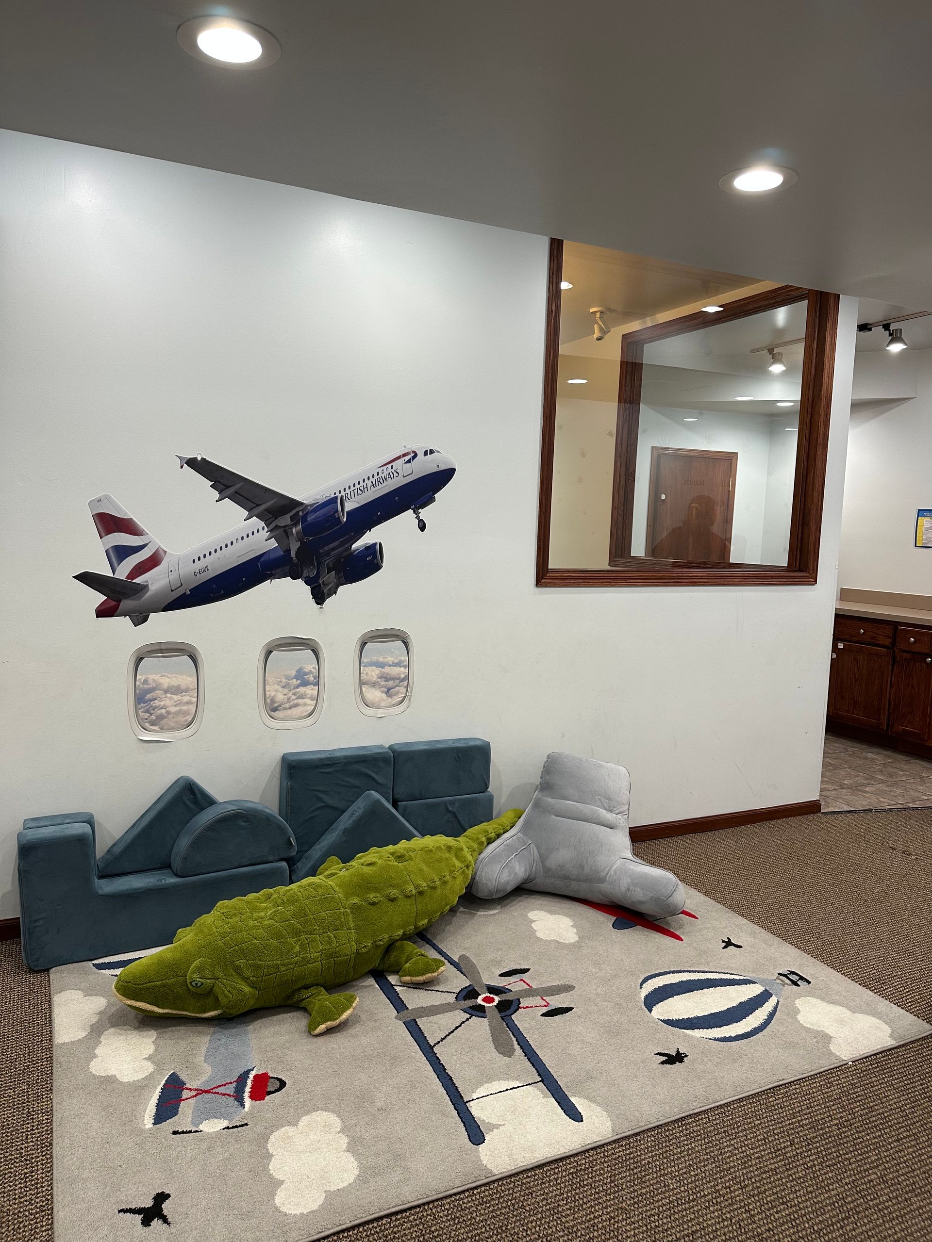 Playroom with plane mural, rug, seating and plush toys.