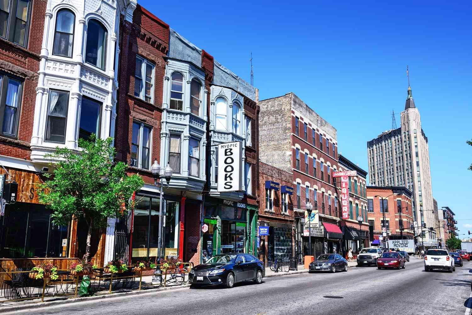Street of historic buildings, bookstore, cars, and tall tower under a clear blue sky.