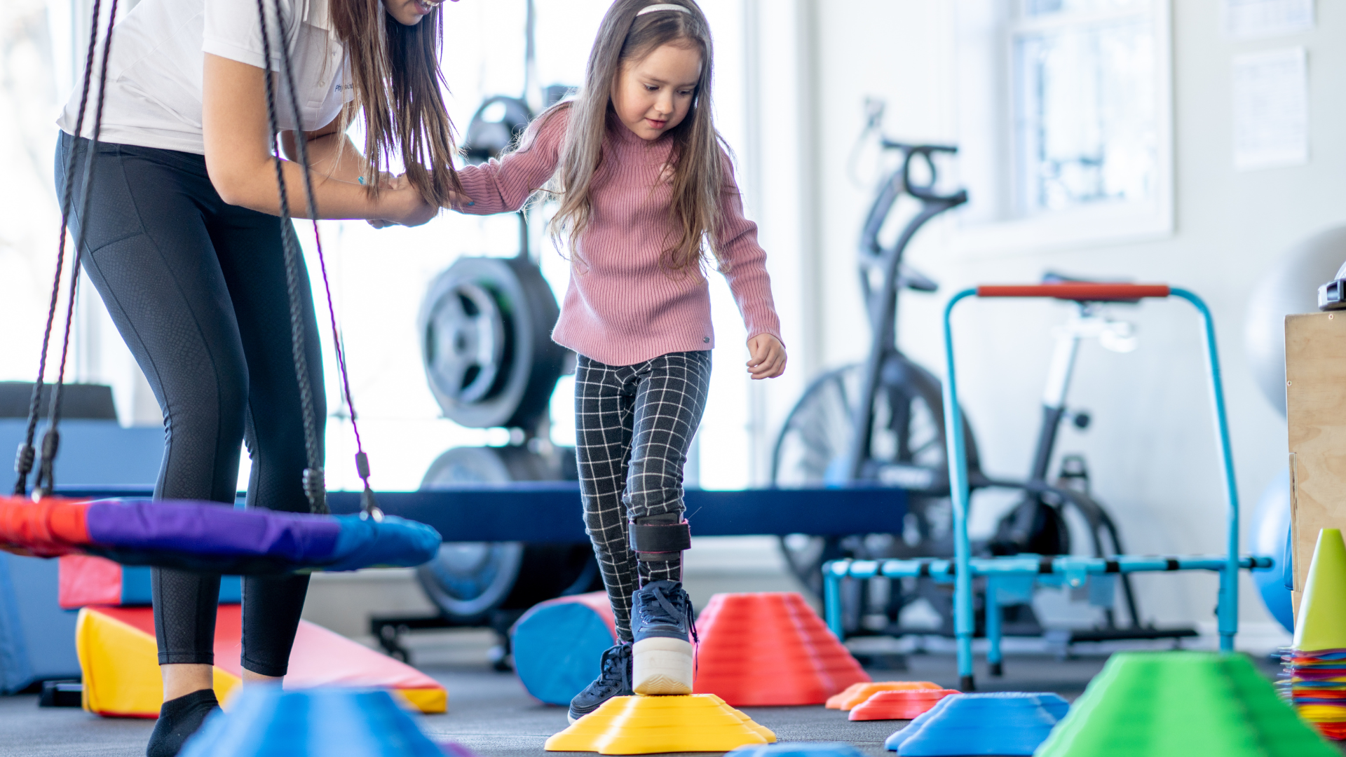 Therapist assists a child walking on cones in a therapy gym, enhancing balance skills.