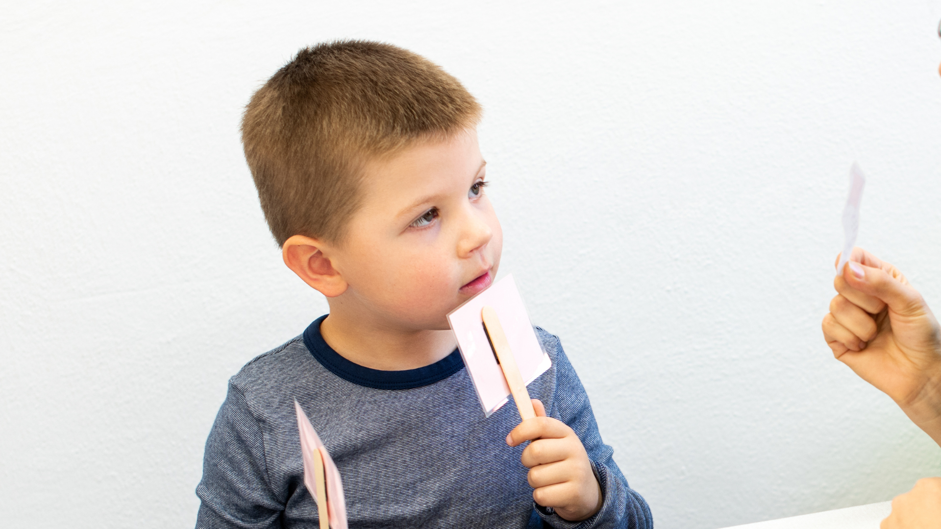 Young child examining cards held by an adult in a brightly lit room.