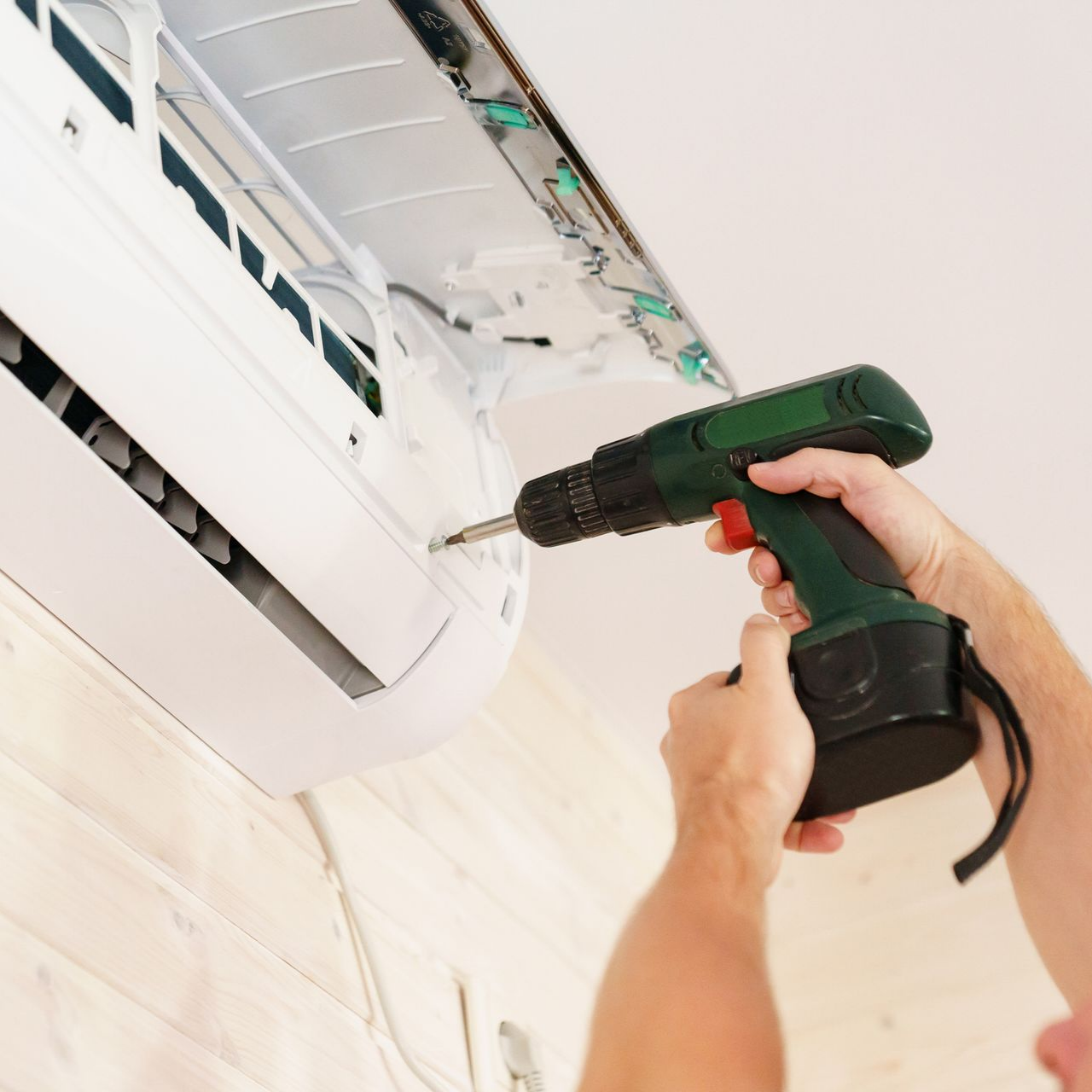 A man uses a screwdriver to remove an air conditioner mounted on the wall. A man uses a screwdriver to remove an air conditioner mounted on the wall.