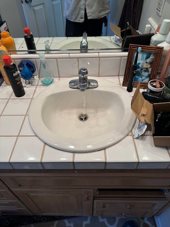 A bathroom sink with a picture of a man in the mirror.