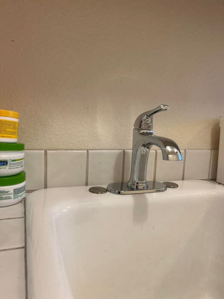 A bathroom sink with a faucet and a stack of jars on the wall.