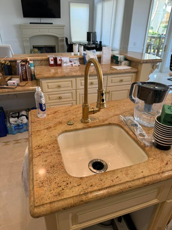 A kitchen sink with a gold faucet on a granite counter top.