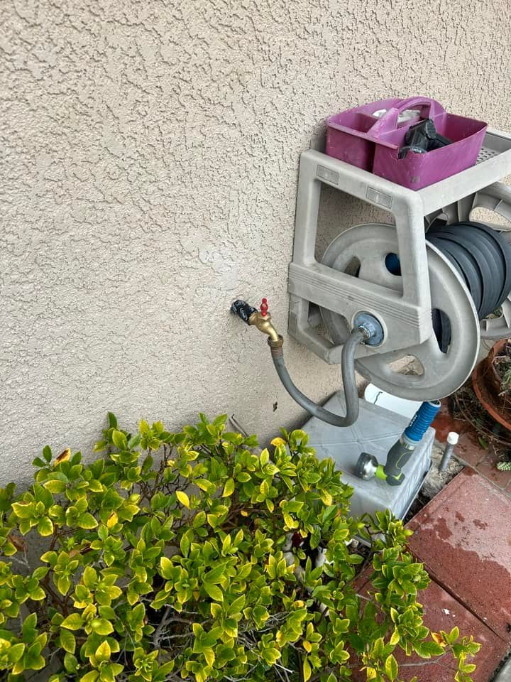 A hose reel is attached to a wall next to a bush.