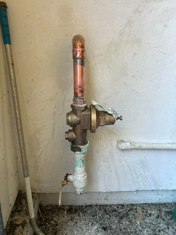 A copper pipe is attached to a wall next to a broom.