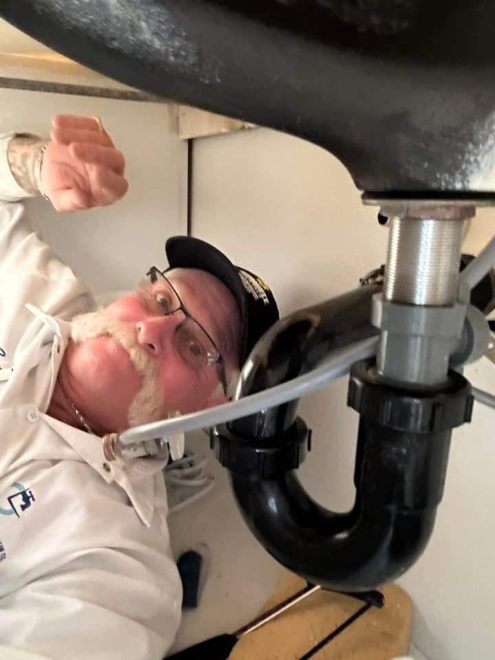 A man wearing glasses and a hat is fixing a sink