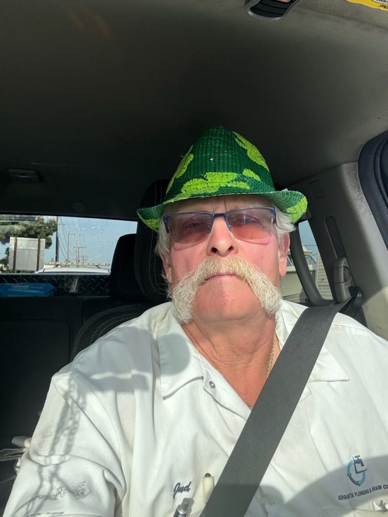 A man with a mustache and a hat is sitting in a car.
