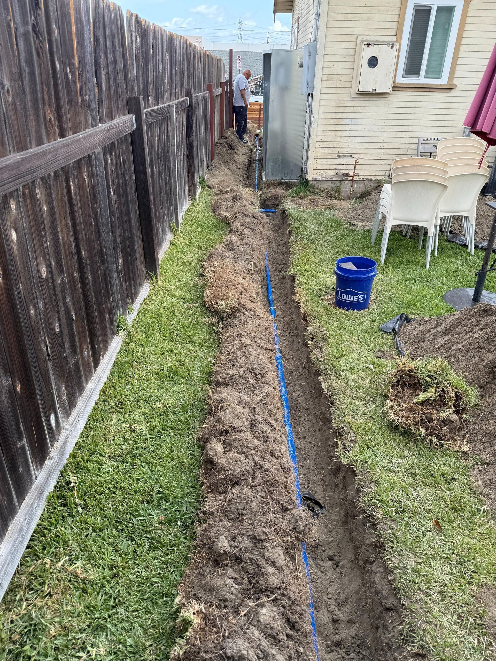 A man is digging a trench in the backyard of a house.