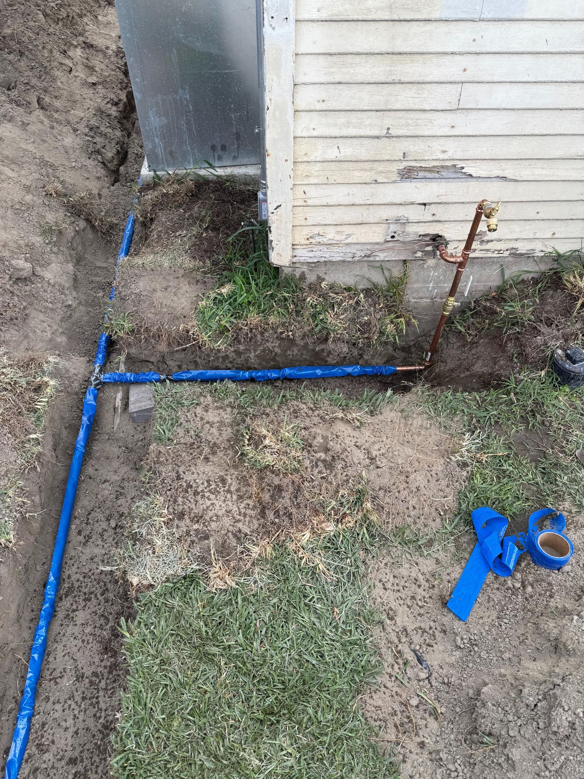 A blue pipe is laying in the dirt next to a house.