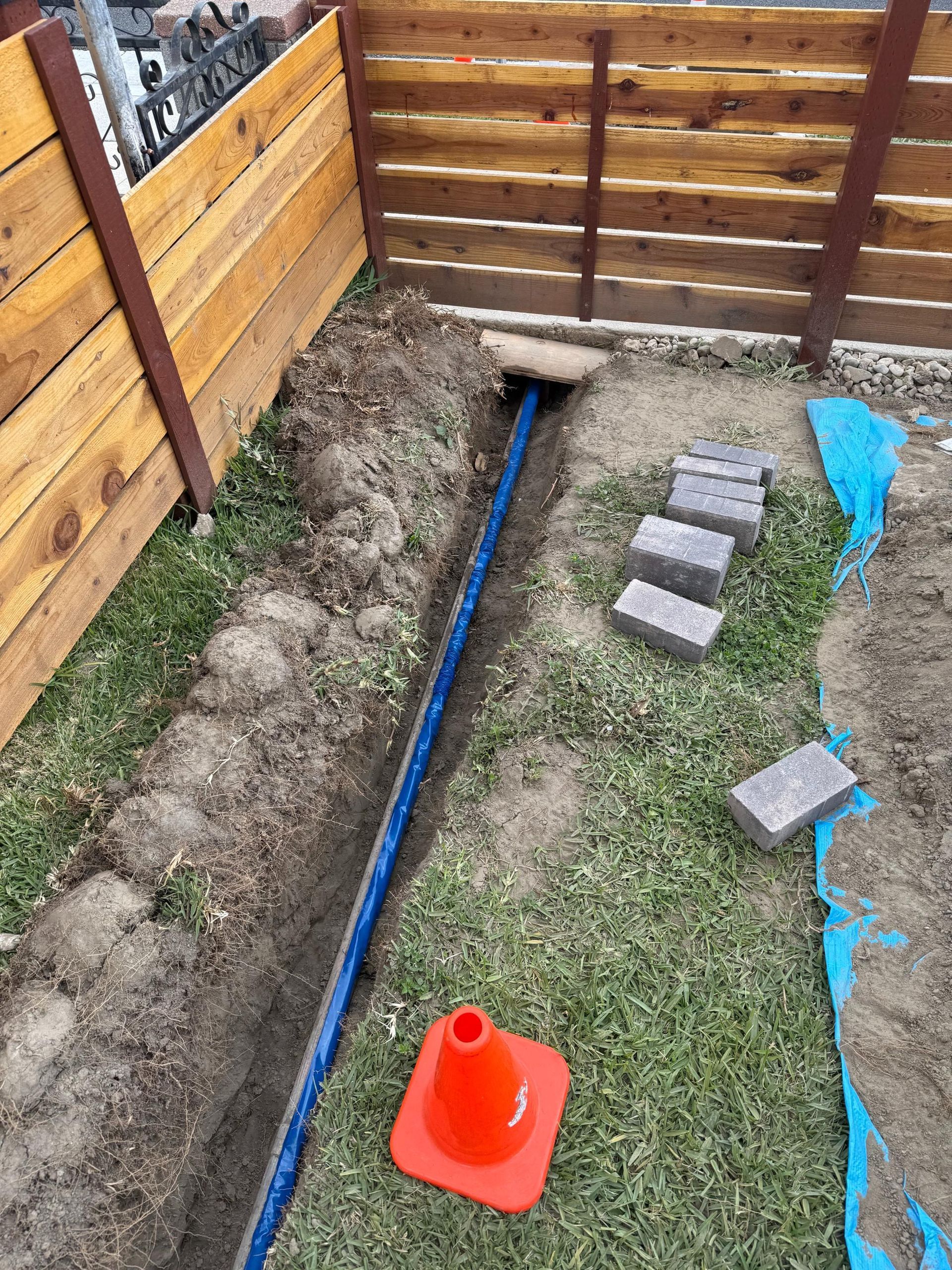A blue pipe is being installed in a yard next to a wooden fence.