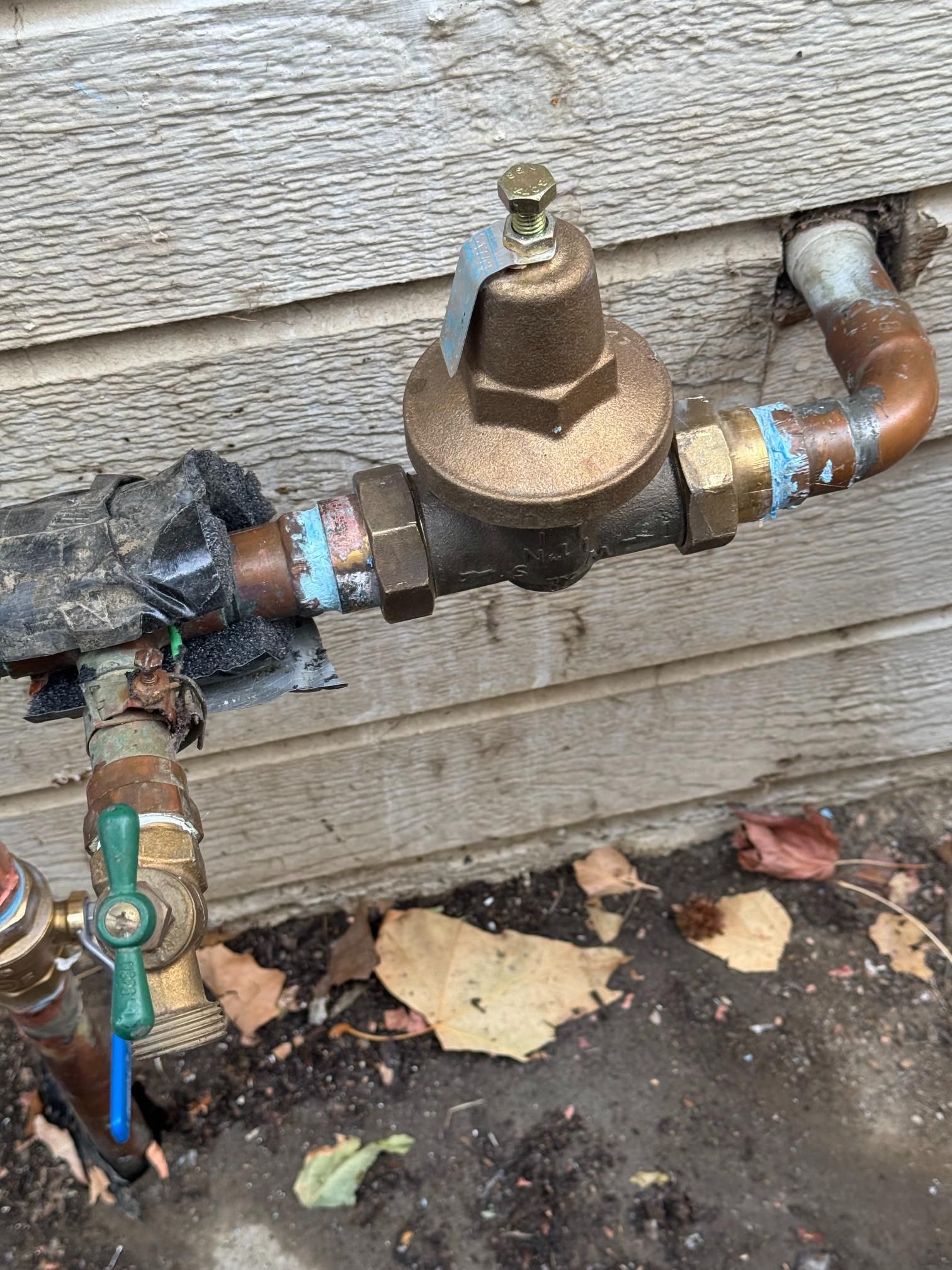 A copper pipe with a valve attached to it is sitting on the ground next to a wooden wall.