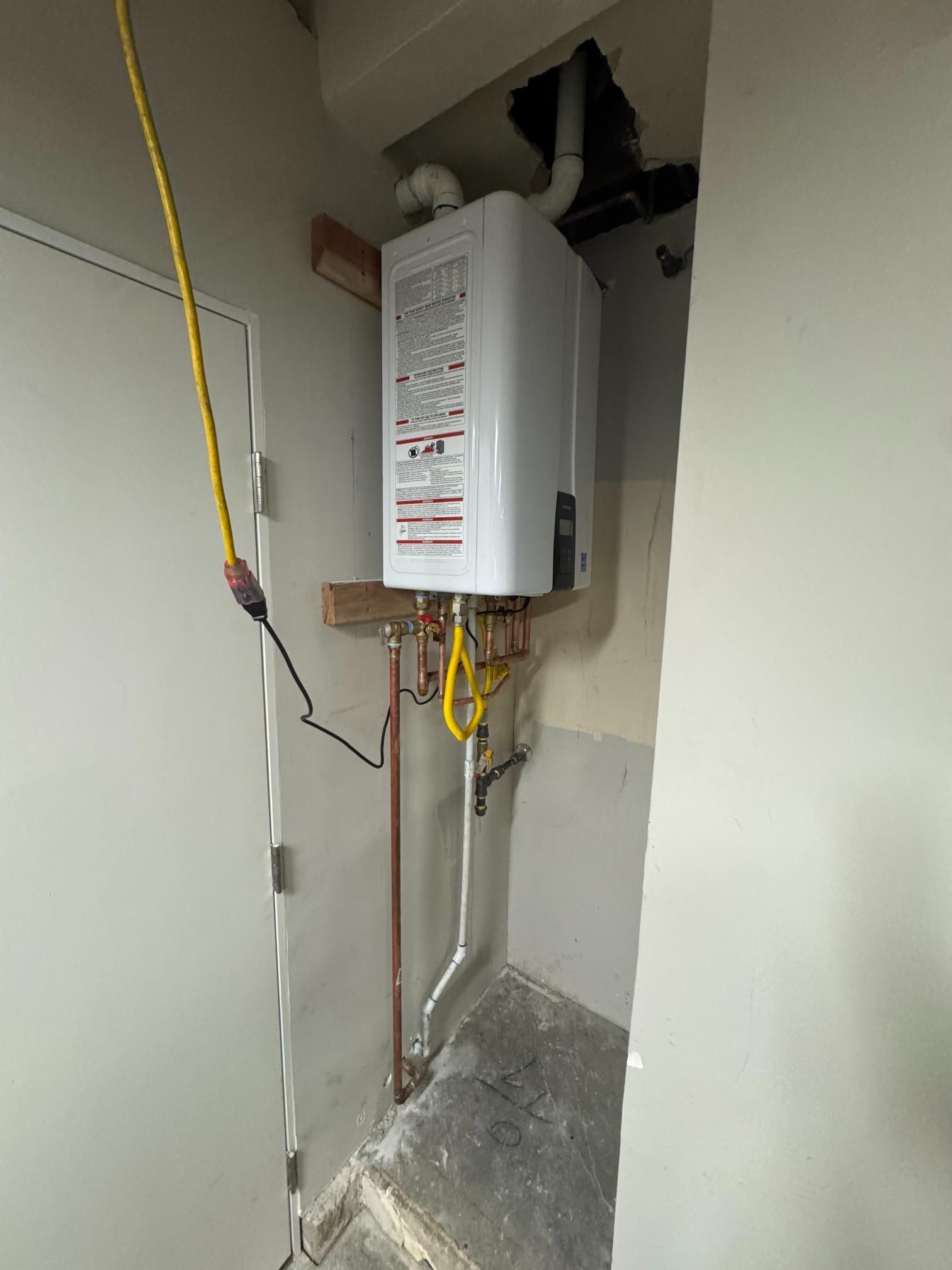 A water heater is hanging from the ceiling in a room next to a door.