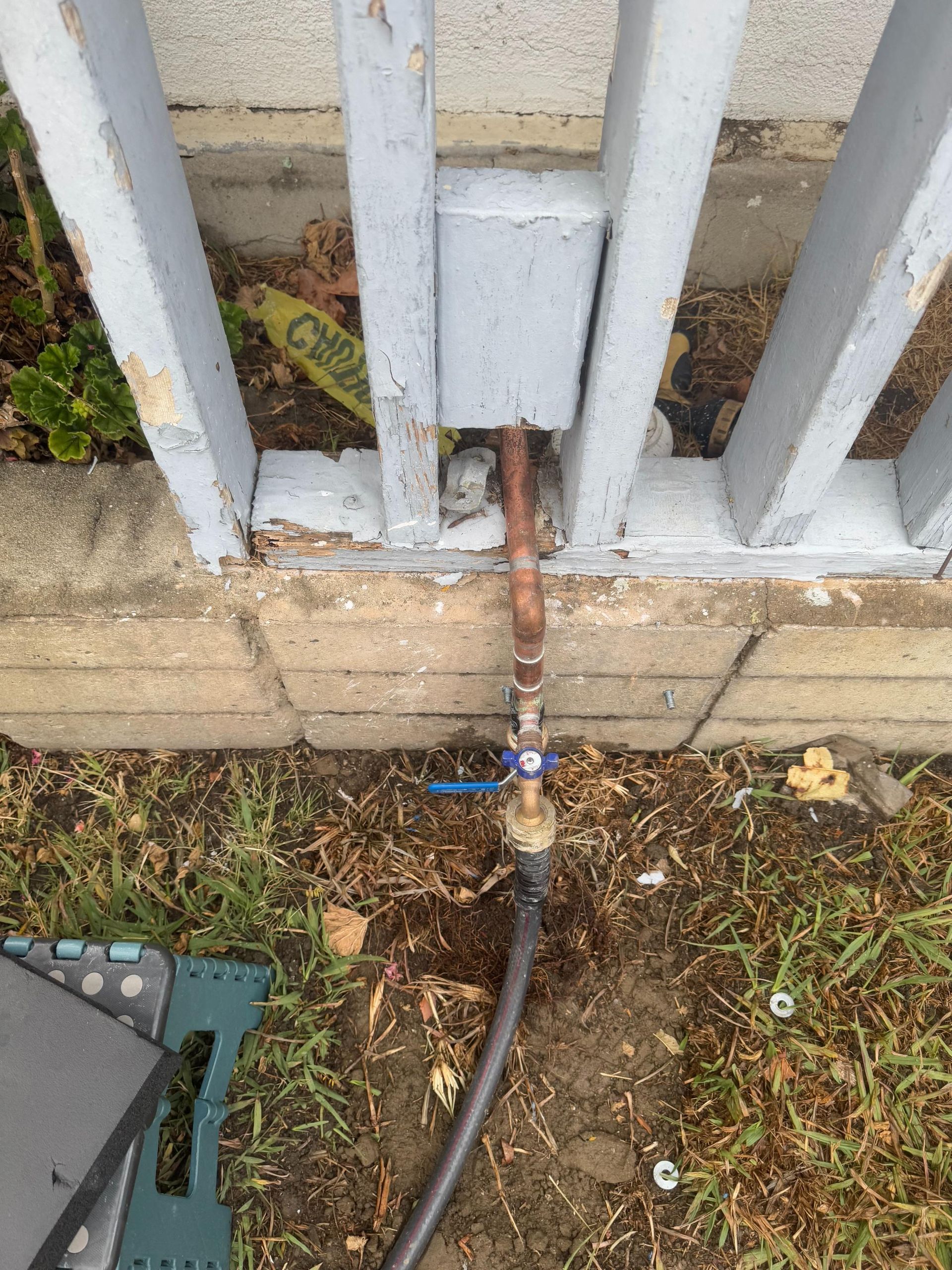 A hose is attached to a metal fence with a blue valve.
