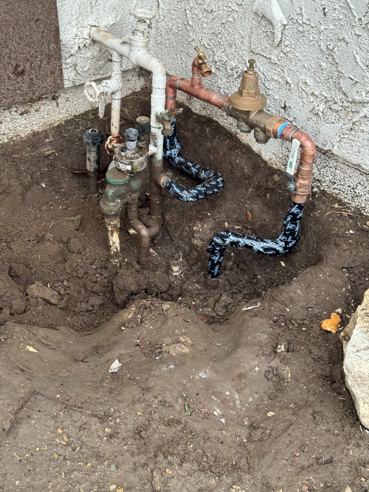 A bunch of pipes are sitting in the dirt next to a wall.