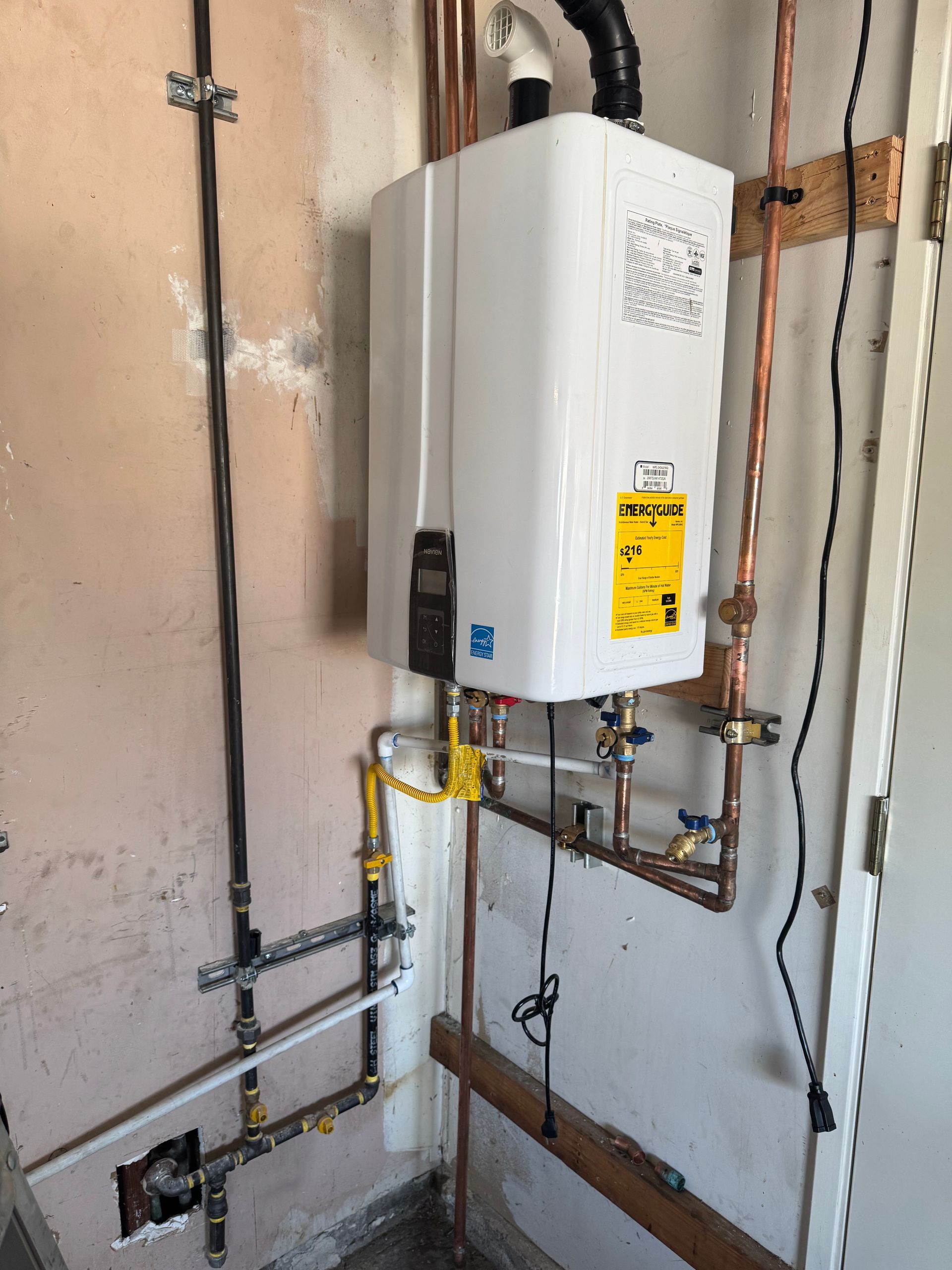 A white water heater is hanging on a wall next to copper pipes.