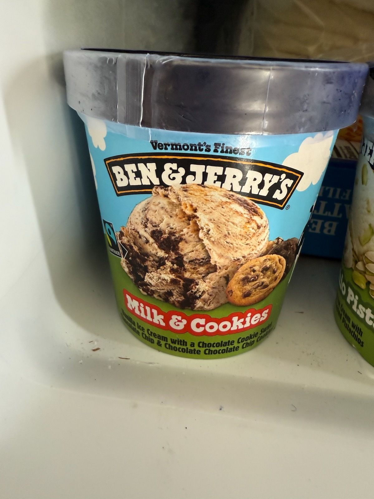 A cup of ben & jerry 's milk and cookies ice cream is sitting on a shelf.